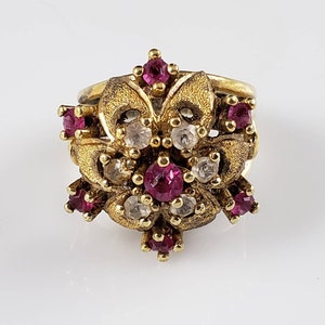 May include: A gold ring featuring a cluster of red and white stones set in a floral design.