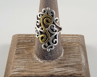 Könnte beinhalten: Ein silberner Ring mit einem goldenen Wirbelmuster. Der Ring befindet sich auf einem hölzernen Ringständer.