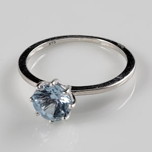 Könnte beinhalten: Ein silberner Ring mit einem hellblauen Edelstein, der in einer Krappenfassung sitzt. Der Ring ist innen mit "STS" gekennzeichnet.
