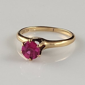 Può includere: Un anello d'oro con un'unica pietra preziosa di rubino rosa brillante rotonda incastonata a griffe.