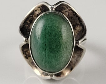 May include: A silver ring featuring an oval, green gemstone. The ring's setting has a textured, floral-like design around the stone. The gemstone is a vibrant shade of green, and the ring is set against a white background.