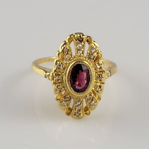 May include: A gold ring with a pink oval gemstone surrounded by smaller diamonds. The ring has a delicate, intricate design.