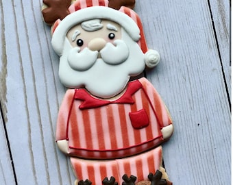 May include: A gingerbread cookie decorated with red and white icing to look like Santa Claus wearing pajamas with reindeer slippers.