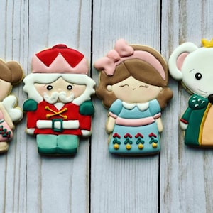 May include: Four decorated sugar cookies featuring characters from the Nutcracker ballet. The cookies are decorated with colorful icing and feature a ballerina, a nutcracker soldier, a mouse king, and Clara.