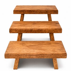 Puede incluir: Un expositor de madera de tres niveles con plataformas rectangulares y un acabado de veta de madera marr&oacute;n medio. Cada nivel est&aacute; sostenido por cuatro patas inclinadas, creando una estructura escalonada que aumenta en altura hacia atr&aacute;s.