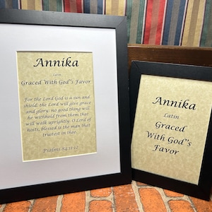 May include: Two framed prints with the name Annika in black lettering on a beige background. The text reads "Annika, Latin, Graced With God's Favor" and includes a Bible verse from Psalms 84:11-12.