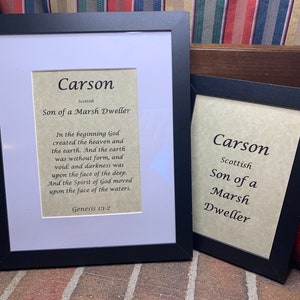 May include: Two framed prints with the name Carson in a black frame. The larger print has the text "Scottish Son of a Marsh Dweller" and a Bible verse from Genesis 1:1-2. The smaller print has the text "Scottish Son of a Marsh Dweller".