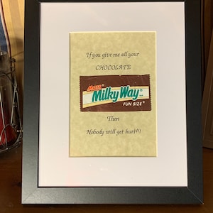 May include: A framed print with a brown and green Milky Way chocolate bar wrapper. The text reads "If you give me all your CHOCOLATE, Then Nobody will get hurt!!!"