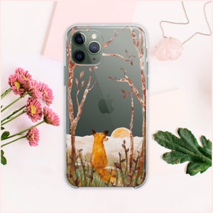 Puede incluir: Una funda transparente para teléfono con un diseño de un zorro de pie en un bosque con árboles y una puesta de sol en el fondo.