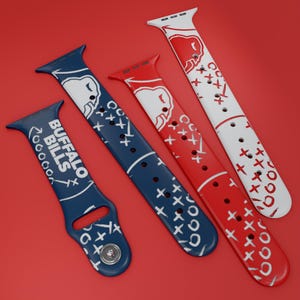 May include: Three silicone watch bands featuring Buffalo Bills branding and football play diagrams. One band is dark blue with white text and graphics, one is red with white graphics, and one is white with red graphics, all showing X and O patterns.