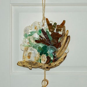 May include: A seashell and driftwood mobile with a white, brown, and green color scheme. The mobile hangs from a white door with a string of small seashells.