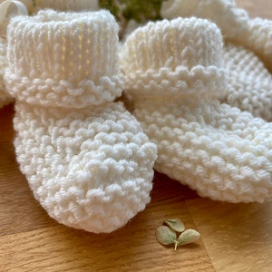 May include: Four pairs of white knitted baby booties with a ribbed texture.