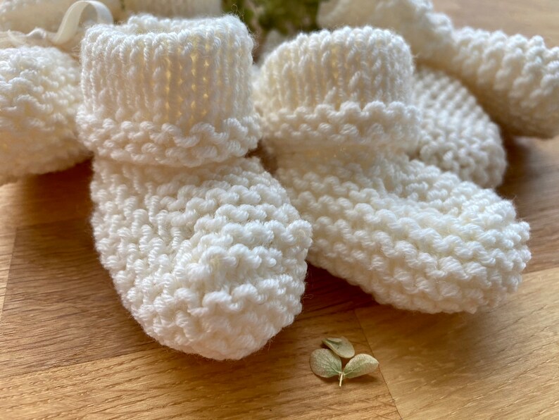 May include: Four pairs of white knitted baby booties with a ribbed texture.