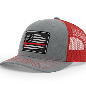 May include: A gray and red trucker hat with a black and white American flag patch featuring a red axe. The patch is sewn onto the front of the hat.
