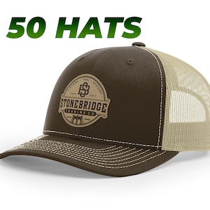 May include: Brown and tan trucker hat with a brown leather patch that says "Stonebridge Trading Co." with a bridge graphic and the letters "SB" inside a circle.