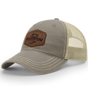 May include: A gray and beige trucker hat with a brown leather patch that says "RIPPIN Lips" and a fish graphic.