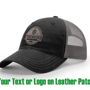May include: Black and gray trucker hat with a leather patch featuring the text "Stonebridge Trading Co." and a logo.