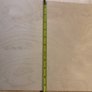 May include: A close-up of a light wood panel with a natural wood grain pattern. A yellow measuring tape is placed vertically along the right edge of the panel. The tape measures 11 inches.