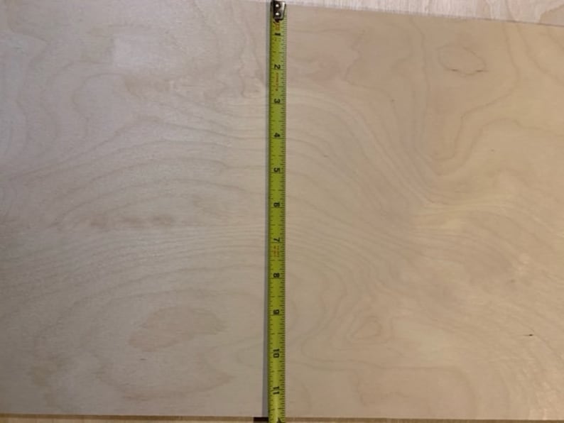 May include: A close-up of a light wood panel with a natural wood grain pattern. A yellow measuring tape is placed vertically along the right edge of the panel. The tape measures 11 inches.