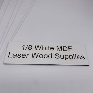 May include: A stack of 1/8 inch thick white MDF sheets. The sheets are smooth and have a white finish. The text "1/8 White MDF Laser Wood Supplies" is printed on a brown label.