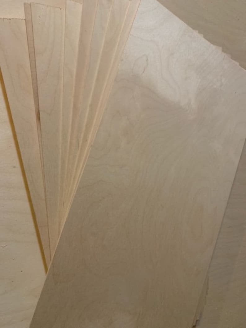 May include: A stack of thin, light wood sheets, likely plywood, with a natural wood grain pattern. The sheets are arranged in a fan shape, with the top sheet extending out to the right.