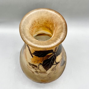 May include: A clear glass vase with a wide mouth and a bulbous body. The vase is decorated with a pattern of brown and gold leaves.