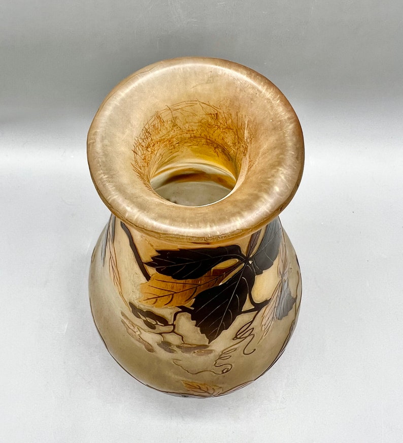 May include: A clear glass vase with a wide mouth and a bulbous body. The vase is decorated with a pattern of brown and gold leaves.