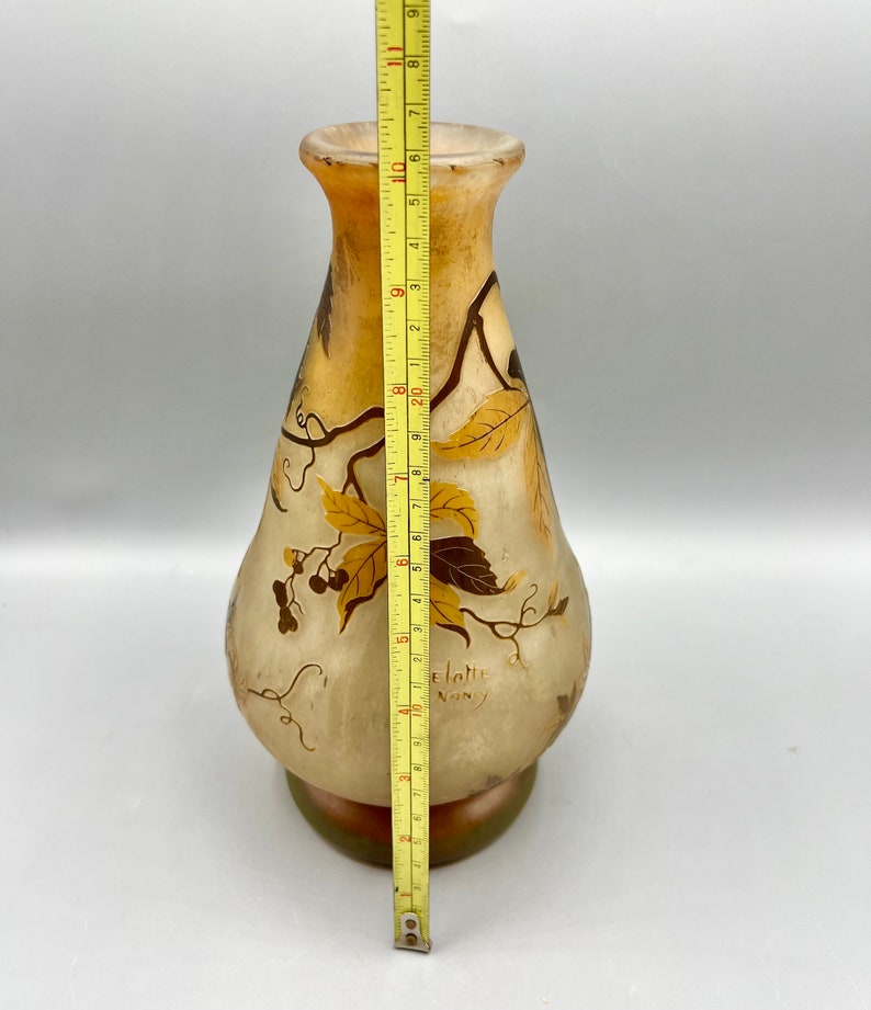May include: A clear glass vase with a brown and gold floral design. The vase is approximately 10 inches tall and has a rounded body with a narrow neck. The vase is signed "Gall&eacute; Nancy".