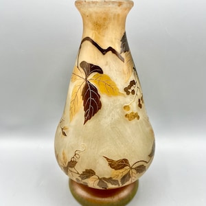 May include: A clear glass vase with a pearlescent finish and a floral design in gold and brown. The vase has a wide base and a narrow neck.