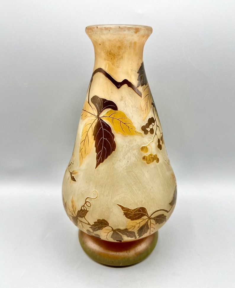 May include: A clear glass vase with a pearlescent finish and a floral design in gold and brown. The vase has a wide base and a narrow neck.
