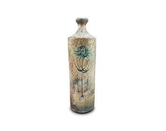 May include: A tall, textured ceramic vase with a narrow neck and a wide base. The vase is primarily beige with a faded blue floral design. The design includes a central flower and several smaller, abstract figures. The vase has a rustic, handcrafted appearance.