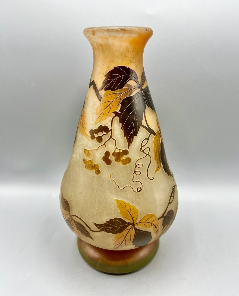 May include: A tall, clear glass vase with a pearlescent finish and a floral design. The vase features a pattern of brown and gold leaves and vines with small, gold berries.