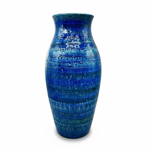 Op de afbeelding: Een hoge, blauwe keramische vaas met een getextureerd oppervlak en een brede opening. De vaas heeft horizontale banden in verschillende blauwtinten, met ingewikkelde witte en turquoise patronen. De vaas is een decoratief item.