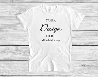 Pode incluir: Uma t-shirt branca de manga curta com o texto impresso a preto YOUR Design HERE e MiracleMockup centrado na zona do peito. A peça tem um decote redondo padrão e uma textura de tecido lisa, apresentada como um modelo de vestuário.