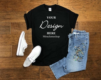 Pode incluir: Uma t-shirt preta de manga curta com o texto branco YOUR Design HERE Miraclemockup impresso na frente, combinada com calças de ganga azuis e um par de ténis brancos com atacadores brancos, dispostos como um conjunto plano.