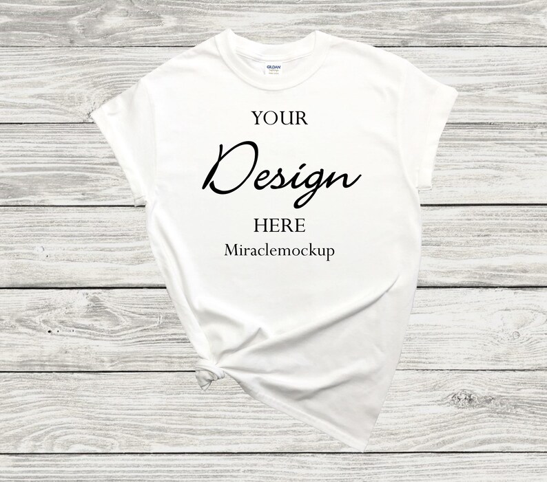 K&ouml;nnte beinhalten: Wei&szlig;es T-Shirt-Mockup mit dem Text "YOUR Design HERE Miraclemockup" auf wei&szlig;em Holz Hintergrund.