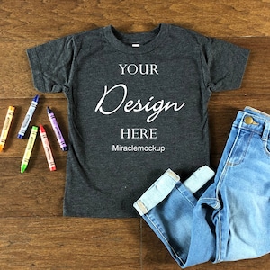 Puede incluir: Una camiseta gris oscuro jaspeada con mangas cortas y cuello redondo. La camiseta tiene el texto "YOUR Design HERE Miraclemockup" impreso en la parte delantera.