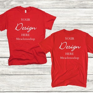 May include: Two red t-shirts with the text "YOUR Design HERE Miraclemockup" on them. The shirts are laid flat on a white wooden surface.