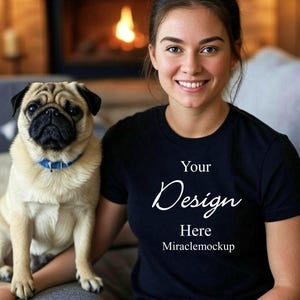 Könnte beinhalten: Schwarzes T-Shirt mit Rundhalsausschnitt und dem Text "Your Design Here Miraclemockup" in weißer Schrift. Ein hellbrauner Mops mit blauem Halsband sitzt neben einer Person. Der Hintergrund umfasst einen Kamin.