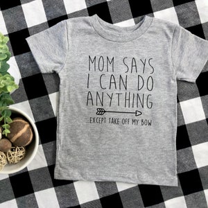 May include: Gray short-sleeved t-shirt with the text "Mom says I can do anything...except take off my bow" and a black arrow pointing to the right.