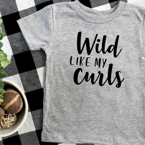 May include: Gray short-sleeved t-shirt with black text that reads "Wild Like My Curls".