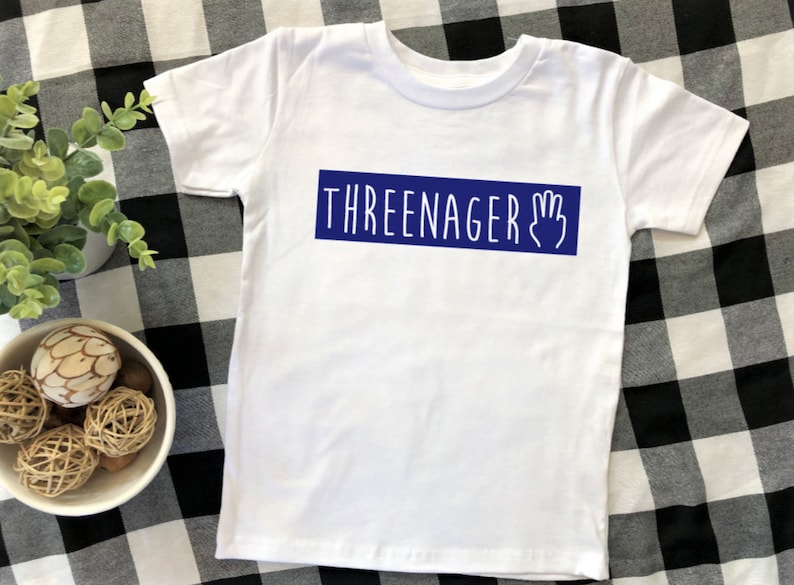 May include: White t-shirt with a blue rectangle that says "THREEENAGER" with a hand drawn three fingered hand.