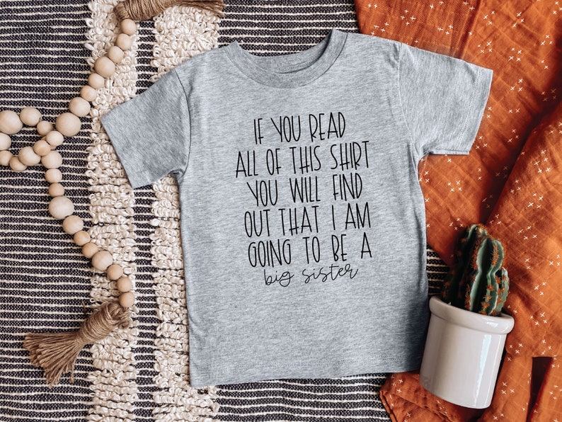 Puede incluir: Camiseta gris de manga corta con texto negro que dice "Si lees toda esta camiseta, descubrir&aacute;s que voy a ser una hermana mayor."