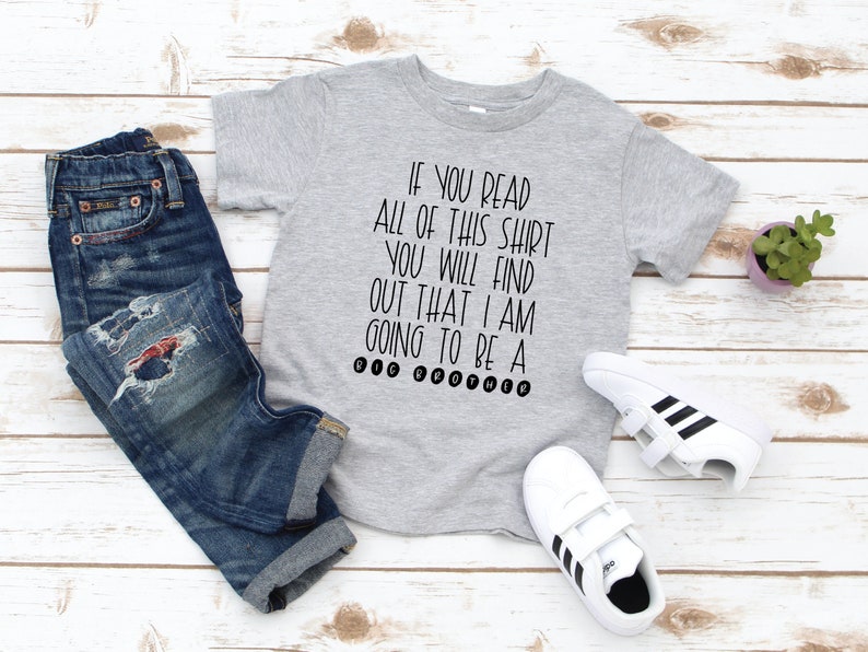 May include: A gray t-shirt with the text "IF YOU READ ALL OF THIS SHIRT YOU WILL FIND OUT THAT I AM GOING TO BE A BIG BROTHER" printed in black.
