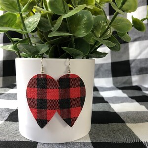 May include: Red and black buffalo plaid teardrop shaped earrings. The earrings are made of leather and have silver hooks.