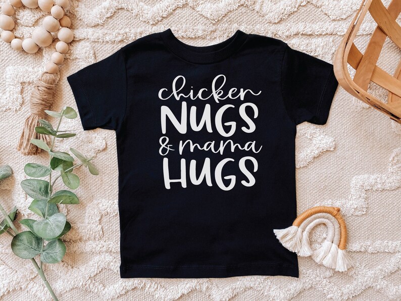 May include: Black t-shirt with white text that reads "chicken NUGS & mama HUGS".