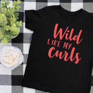 May include: Black t-shirt with the text "Wild Like My Curls" in red lettering.