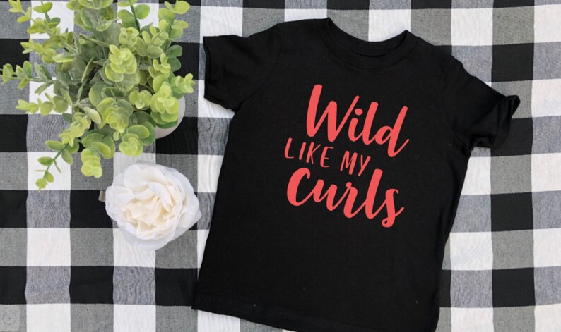 May include: Black t-shirt with the text "Wild Like My Curls" in red lettering.