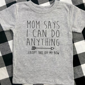 May include: Gray t-shirt with black text that reads "Mom says I can do anything... except take off my bow" with a black arrow pointing to the right.