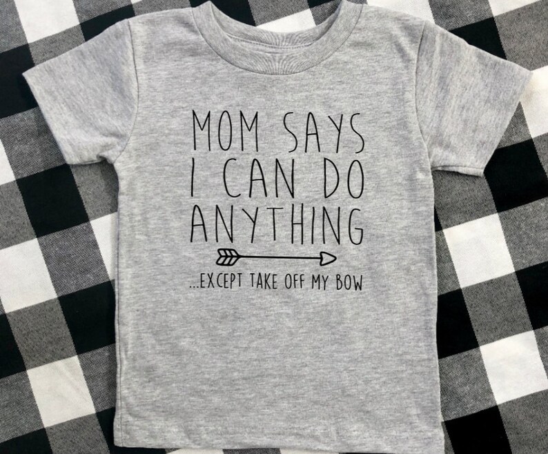May include: Gray t-shirt with black text that reads "Mom says I can do anything... except take off my bow" with a black arrow pointing to the right.